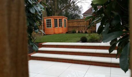 back garden with porcelain paving in the foreground with a lawn and summerhouse in the background