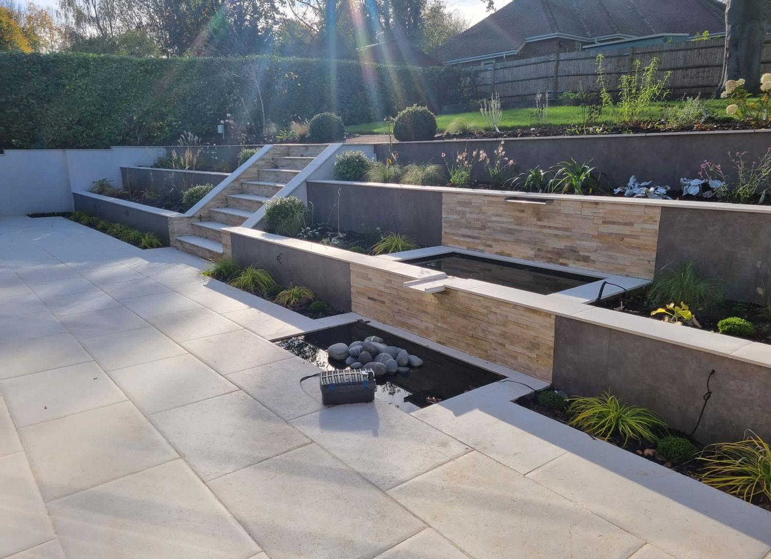 lovely english country garden with patio, water feature and retaining walls with steps to upper terrace