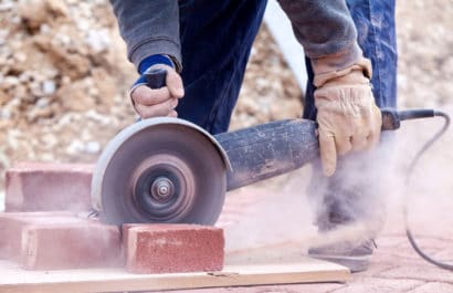 hiring a landscaper might mean dust and noise! image of a landscaper cutting clay pavers to size